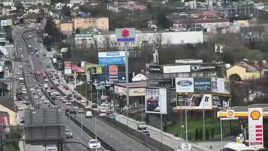 A multi-lane highway with moderate traffic flows past numerous billboards and buildings on an overcast day.