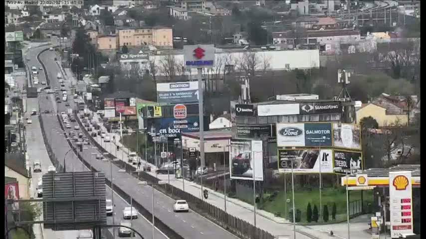 A highway with moderate traffic flows through a city with numerous billboards and buildings on a cloudy day.