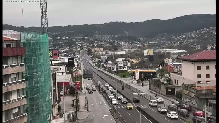 A partly cloudy day reveals a highway with moderate traffic passing through a city nestled at the base of a mountain range.