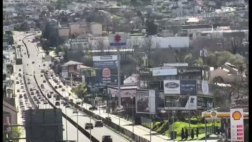 A highway with moderate traffic flows through a city on a sunny day.