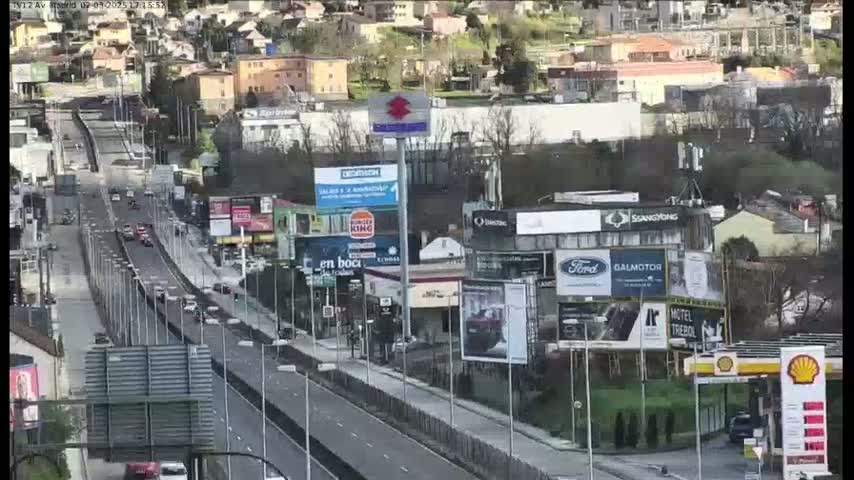 A highway with moderate traffic flows through a city with numerous buildings and billboards, on an overcast day.