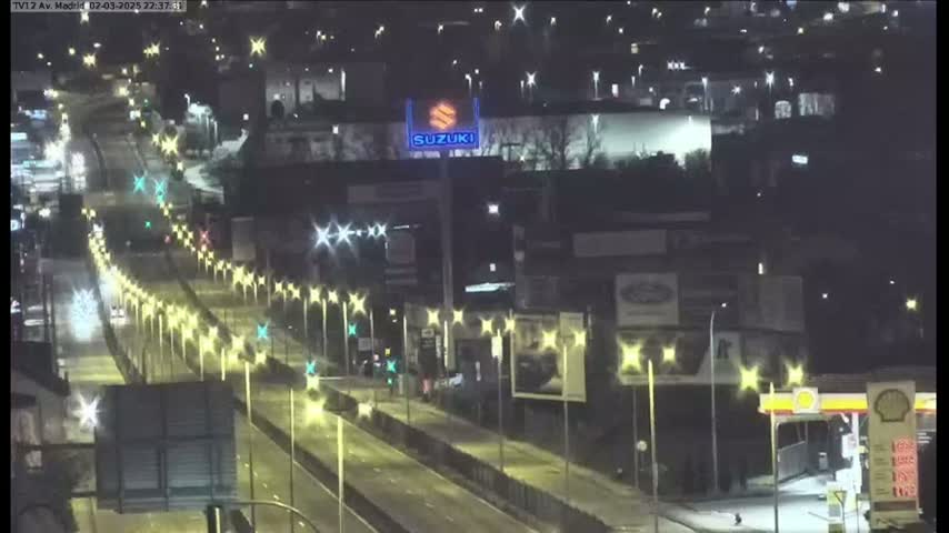 A nighttime, brightly lit highway scene shows a multi-lane road with sparse traffic, lined with light posts, and buildings along the sides.