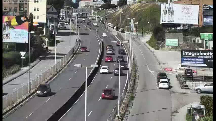 A sunny day reveals a multi-lane highway with moderate traffic flowing in both directions, surrounded by buildings and roadside advertisements.