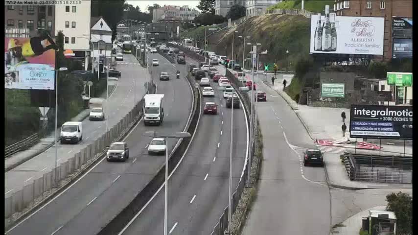 A multi-lane highway with moderate traffic flows through a cityscape under overcast skies.