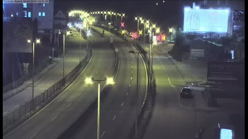 A multi-lane highway at night with a few cars driving, illuminated by streetlights, under a clear, dark sky.