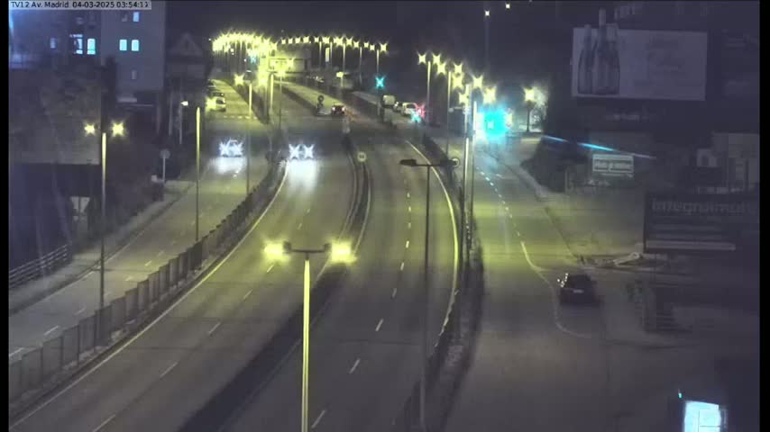 A nighttime, slightly wet highway scene shows several cars driving on a multi-lane road illuminated by streetlights.
