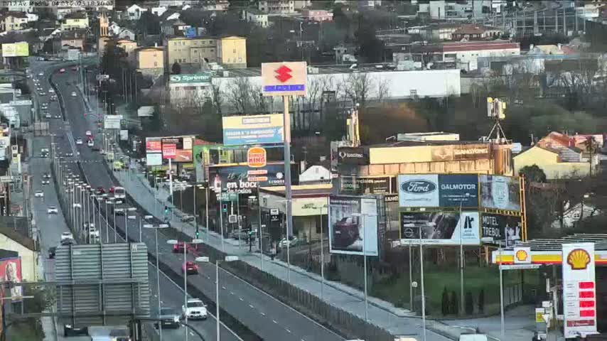 A highway with moderate traffic flows through a city with numerous billboards and buildings under a partly cloudy sky.