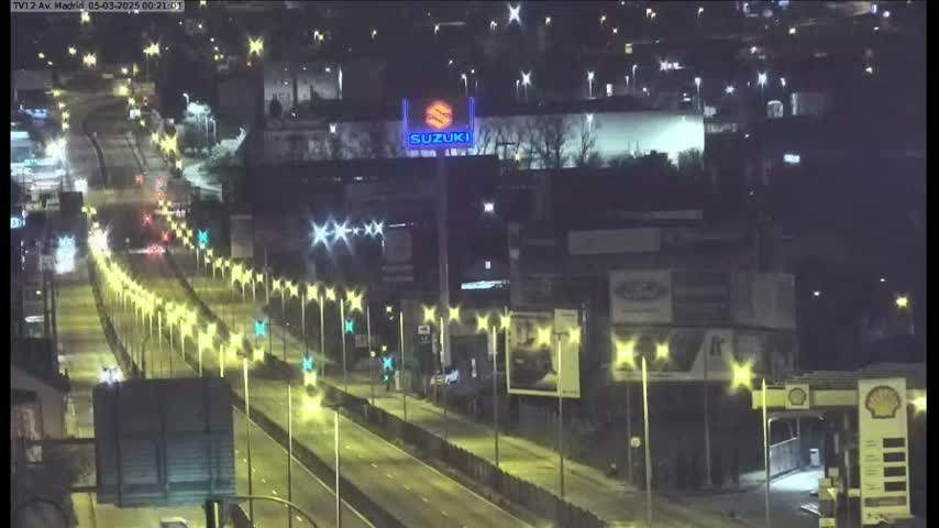 A nighttime, brightly lit highway scene with sparse traffic and a Suzuki dealership visible in the background.