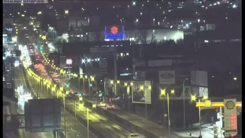 A nighttime aerial view shows a busy highway with moderate traffic under partly cloudy skies.