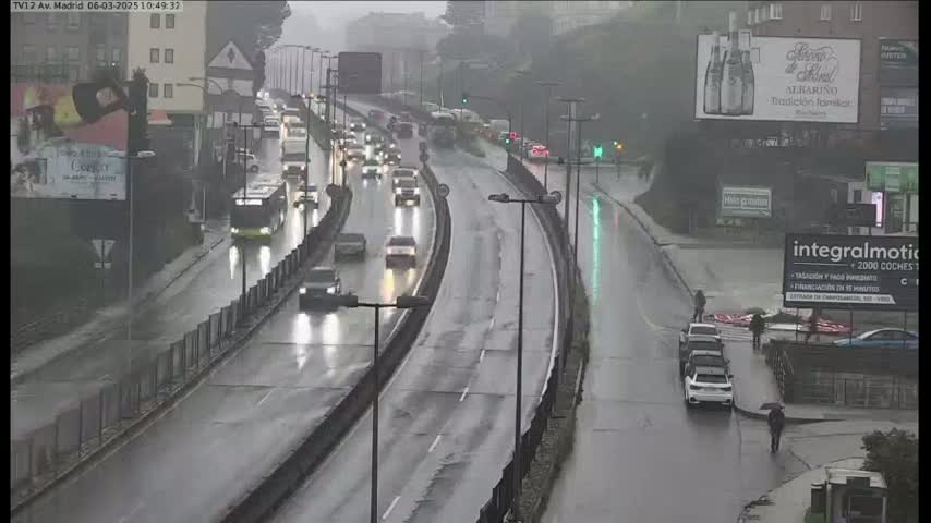 A rain-slicked highway curves through a city, with cars and a bus traveling in both directions amidst heavy rainfall.