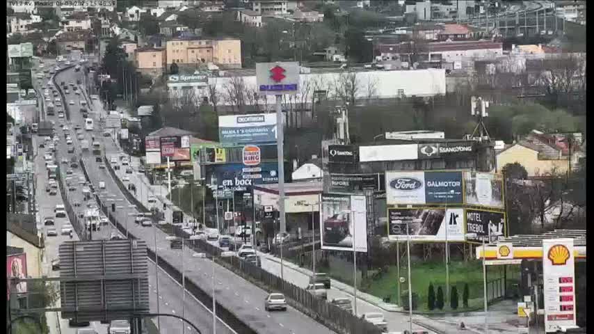 A highway with heavy traffic flows past billboards and buildings on an overcast day.