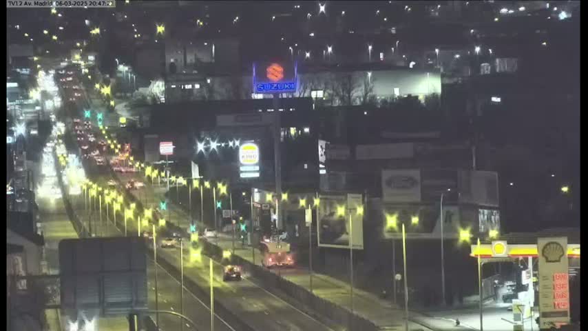 A nighttime, high-angle view of a multi-lane highway with heavy traffic flowing through a city, illuminated by streetlights.