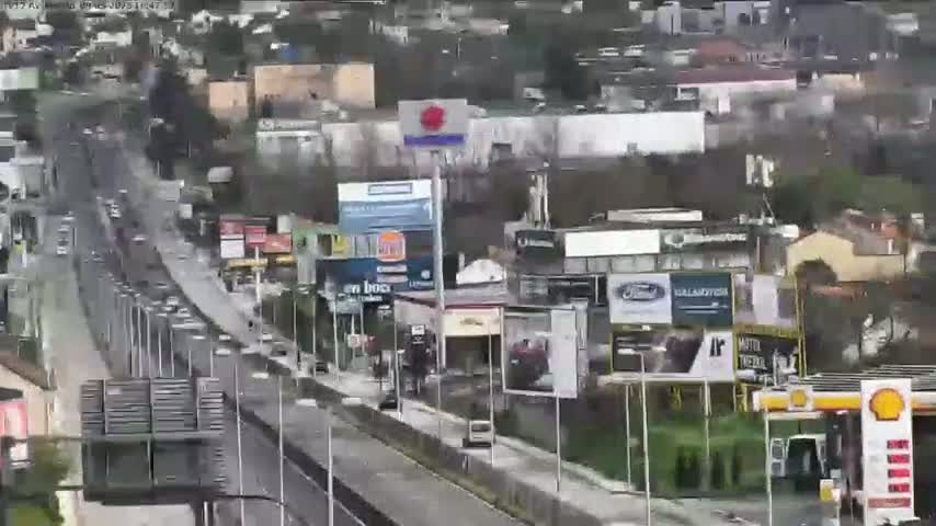 A highway with heavy traffic flows past numerous billboards and businesses on an overcast day.