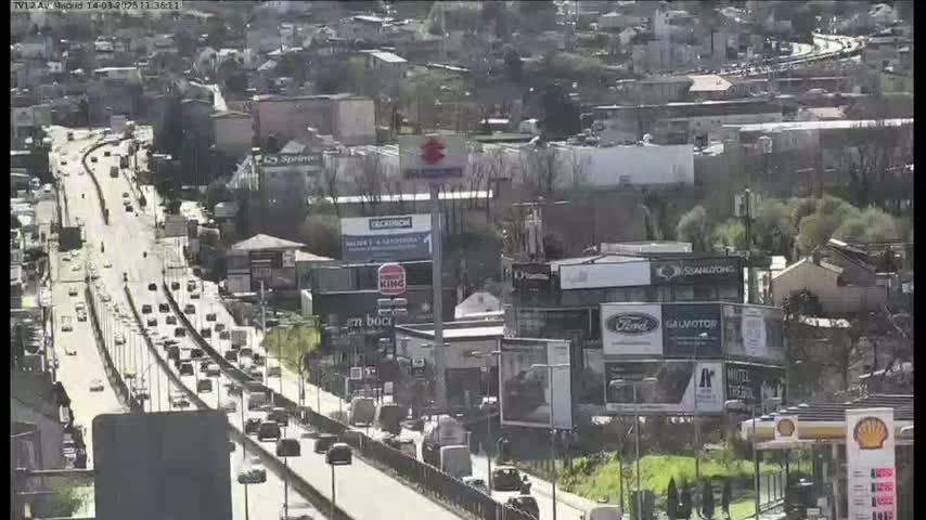 A highway with moderate traffic flows past businesses and buildings on a sunny day.
