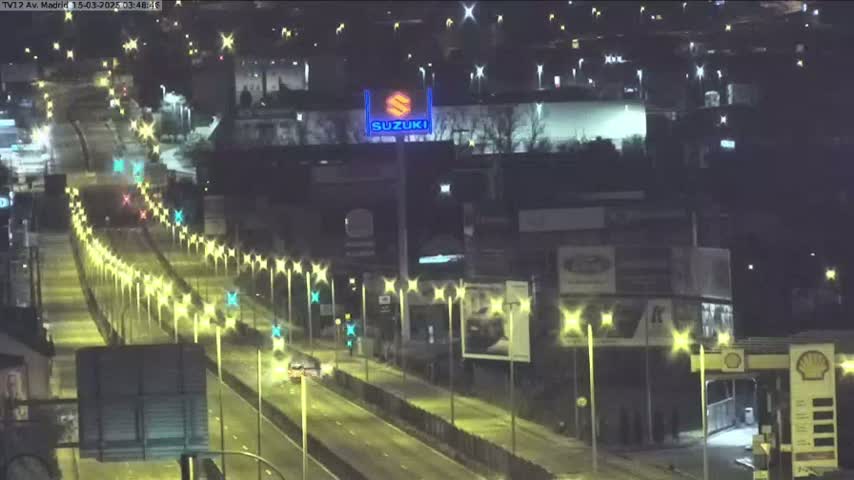 A nighttime, well-lit highway scene shows sparse traffic and buildings along the sides.