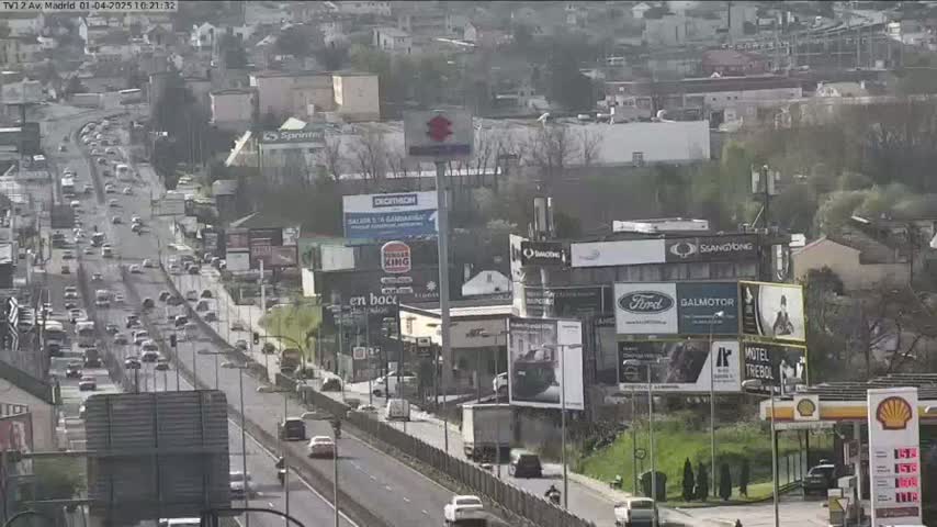 A highway with heavy traffic flows past billboards and buildings on a partly cloudy day.