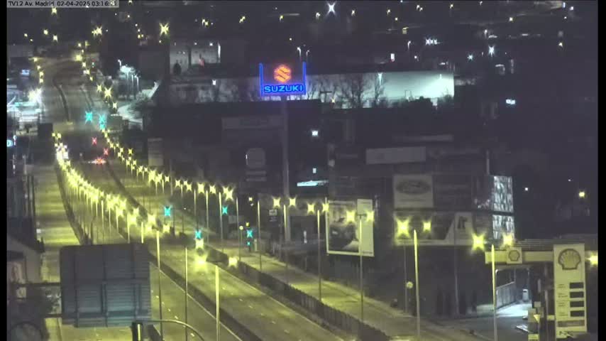 A nighttime, brightly-lit highway scene shows several vehicles traveling on a multi-lane road lined with streetlights, passing by buildings and advertisements.