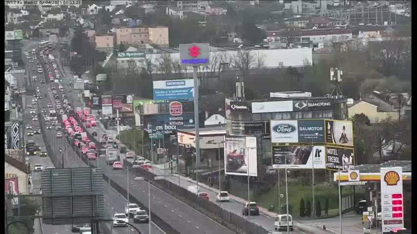 A heavily congested highway with numerous cars, including a long line of red cars, under an overcast sky.
