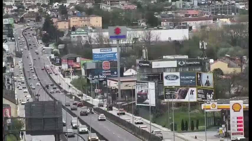 A multi-lane highway with moderate traffic flows through a city with numerous billboards and buildings, under a mostly clear sky.