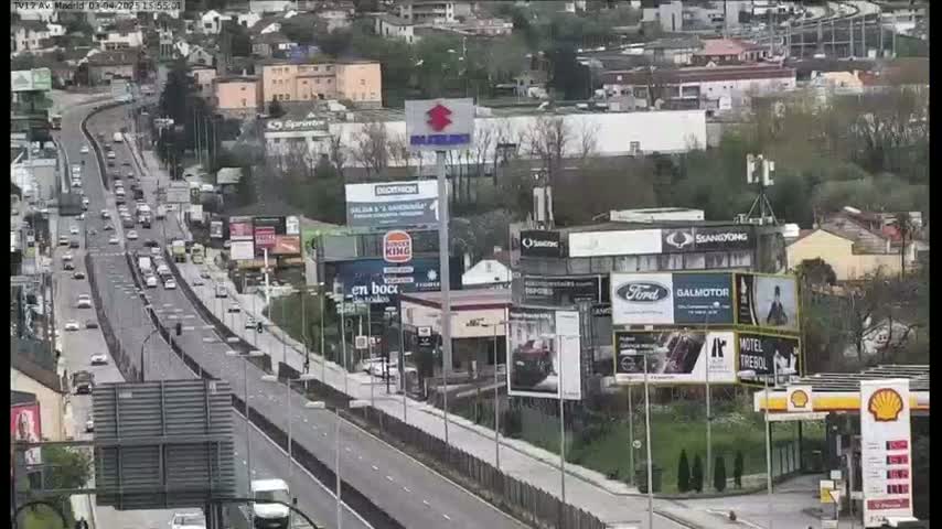 A highway with moderate traffic flows past buildings and billboards on an overcast day.