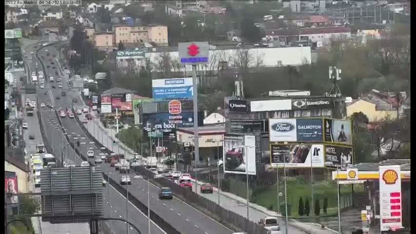A multi-lane highway with moderate traffic flows through a city on an overcast day, lined with billboards and businesses.