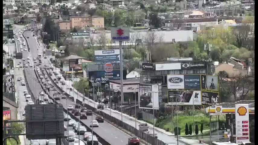 A congested highway scene, under a seemingly overcast sky, shows numerous vehicles traveling through a city with various buildings and billboards lining the road.