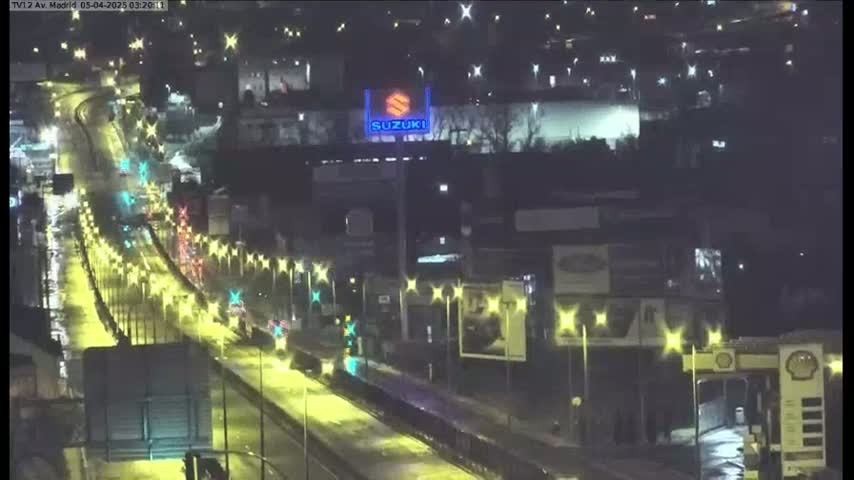 A wet, nighttime highway scene shows a multi-lane road with cars driving under illuminated streetlights.