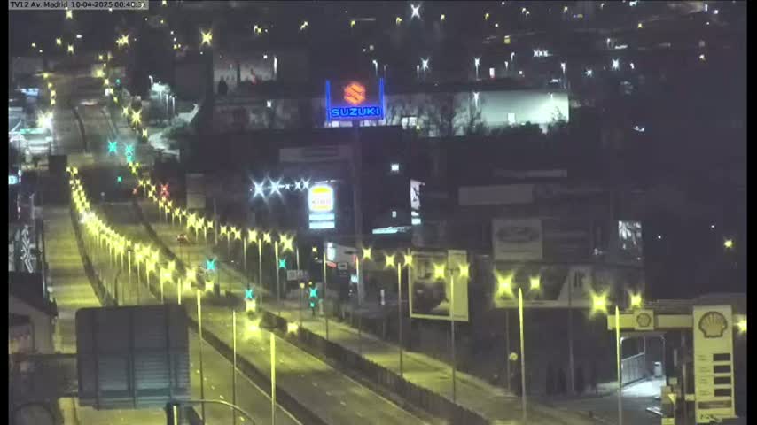 A nighttime view of a multi-lane highway with sparse traffic, lined with streetlights, and buildings with illuminated signs in the background.