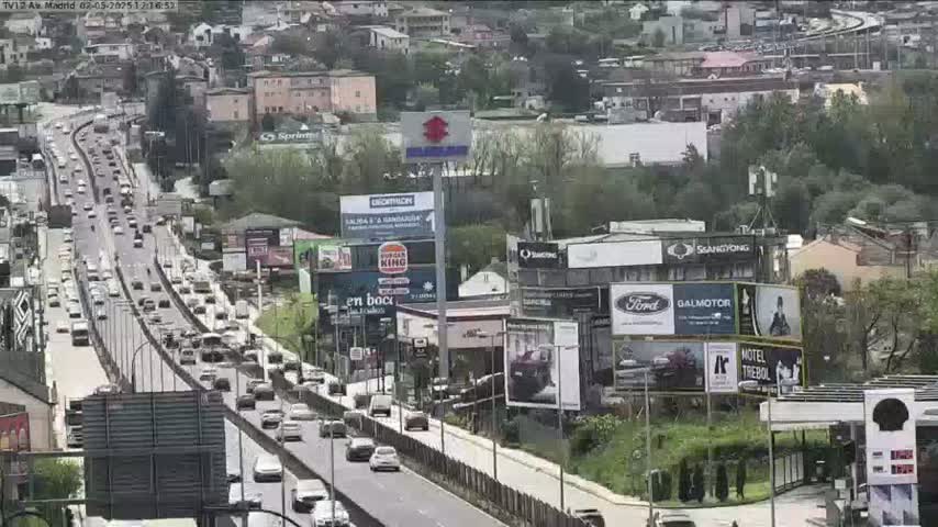 A highway scene shows many cars driving on a multi-lane road that passes through a city with numerous billboards and buildings, on an overcast day.