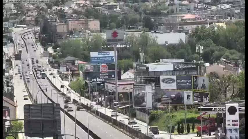 A highway with moderate traffic flows through a city on a partly sunny day, with numerous billboards and buildings lining the roadside.