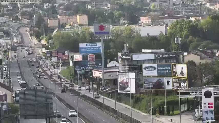 A highway scene shows moderate traffic moving in both directions, with numerous billboards and advertisements lining the roadside on a partly cloudy day.