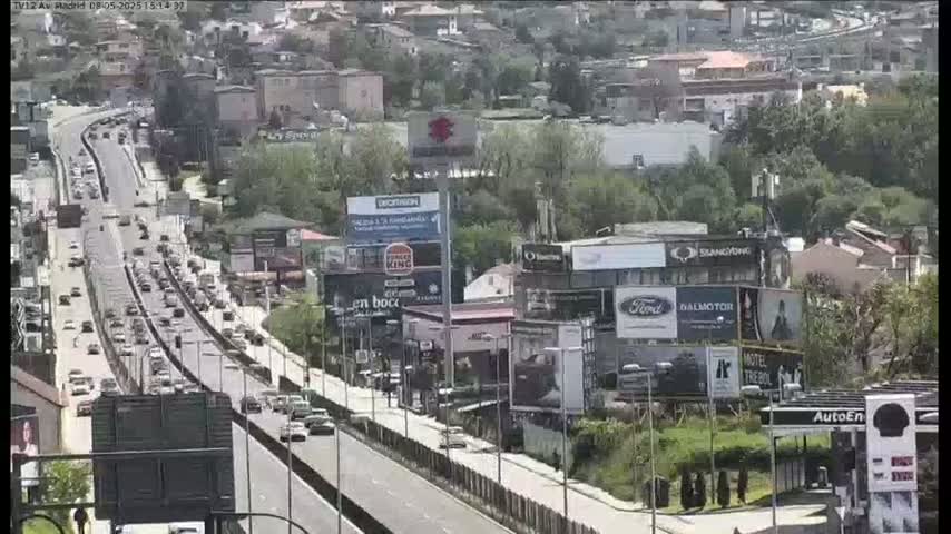 A multi-lane highway with heavy traffic flows through a cityscape on a partly sunny day.
