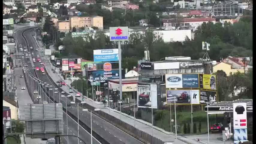 A highway with moderate traffic flows through a city on an overcast day, passing numerous billboards and buildings.