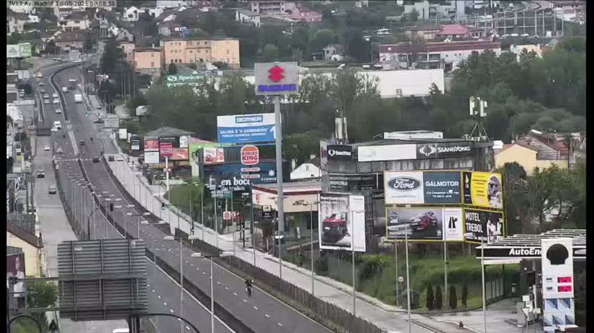 A multi-lane highway stretches through a cityscape under an overcast sky, lined with billboards and buildings.