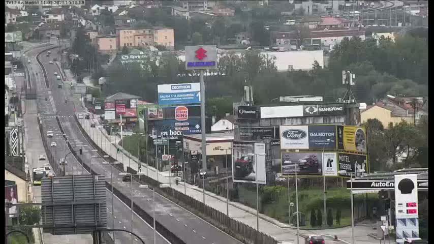 A highway scene on an overcast day shows a multi-lane road with light traffic, surrounded by billboards and buildings.