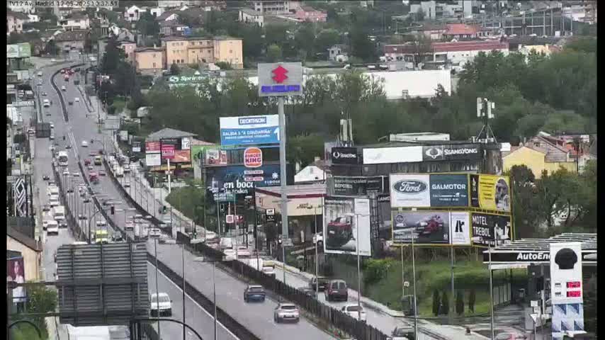 A multi-lane highway, busy with cars, is seen from an elevated view on an overcast day, surrounded by buildings and billboards.