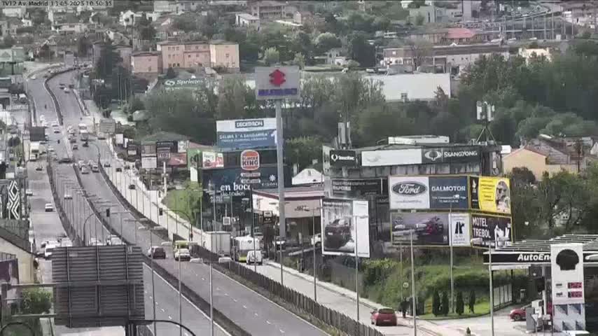 A highway with moderate traffic flows through a city on an overcast day, lined with billboards and businesses.