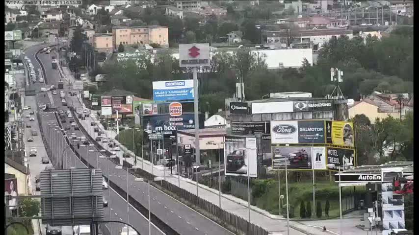 A highway with moderate traffic flows through a city on an overcast day, lined with billboards and businesses.