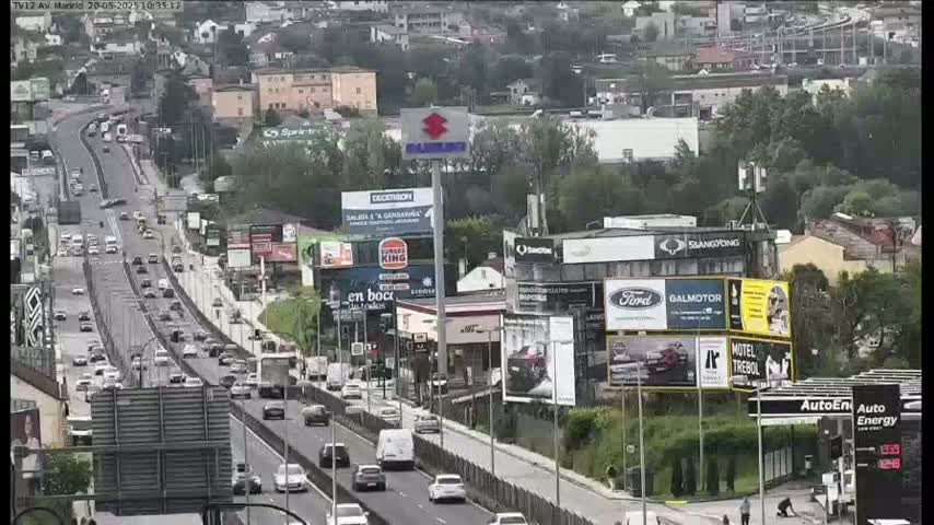 A multi-lane highway with moderate traffic flows through a city under partly cloudy skies.