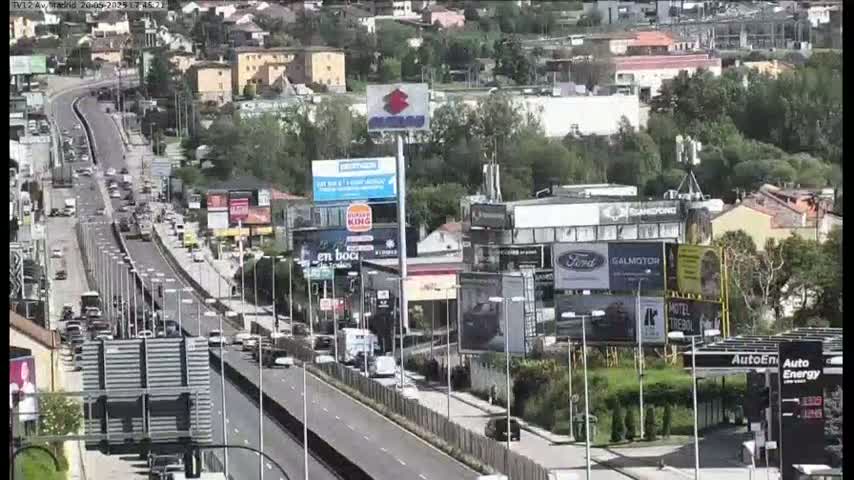 A highway scene on a sunny day shows moderate traffic moving through a city area with numerous billboards and businesses along the roadside.