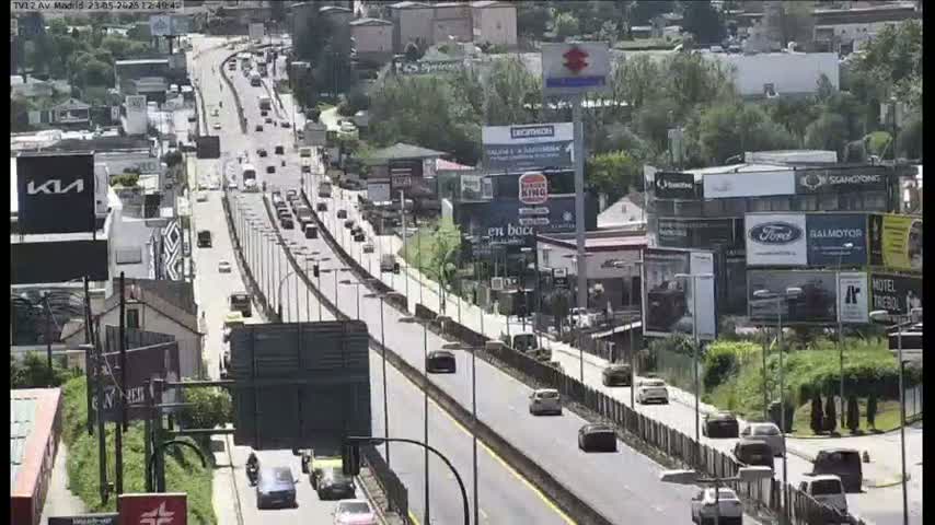 A multi-lane highway with moderate traffic flows through a city, under a mostly sunny sky.