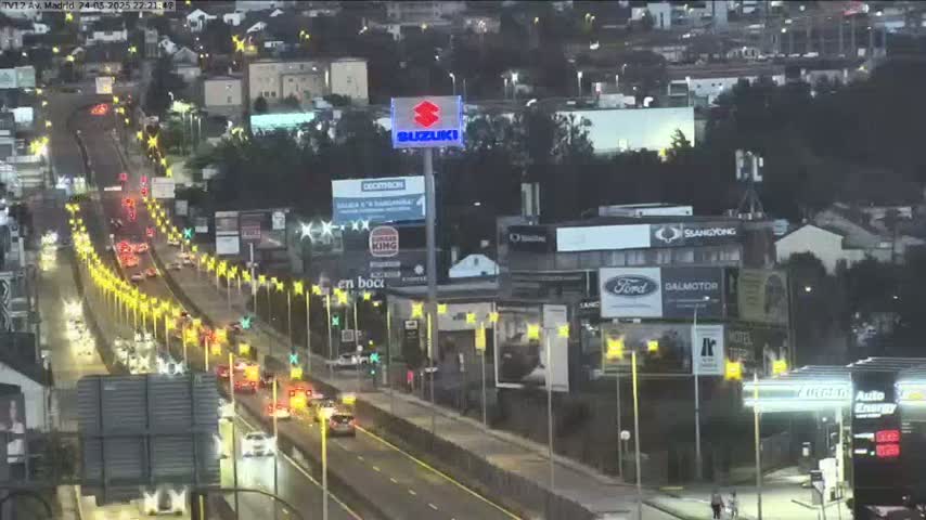 A wet highway at night with moderate traffic flows past buildings with illuminated advertisements and streetlights.