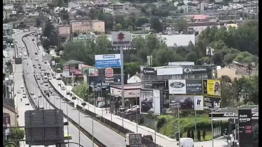 A highway with moderate traffic flows through a city landscape under a clear sky.