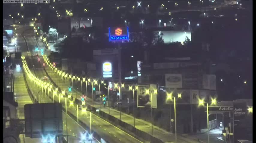 A rain-slicked highway at night is lined with evenly spaced streetlights, with vehicles driving along it, and a Suzuki billboard visible in the background.