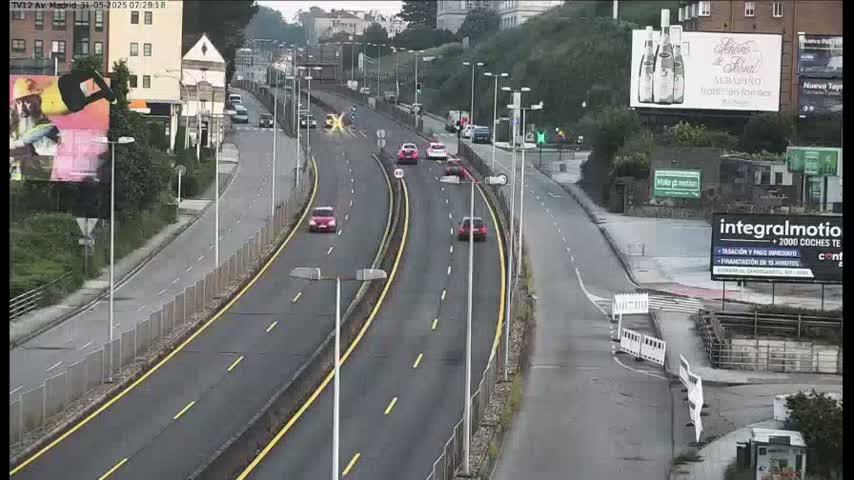 A multi-lane highway curves gently, with a few cars driving on it, under an overcast sky.