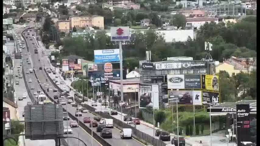 A highway with moderate traffic flows through a city on a partly cloudy day, passing numerous billboards and buildings.