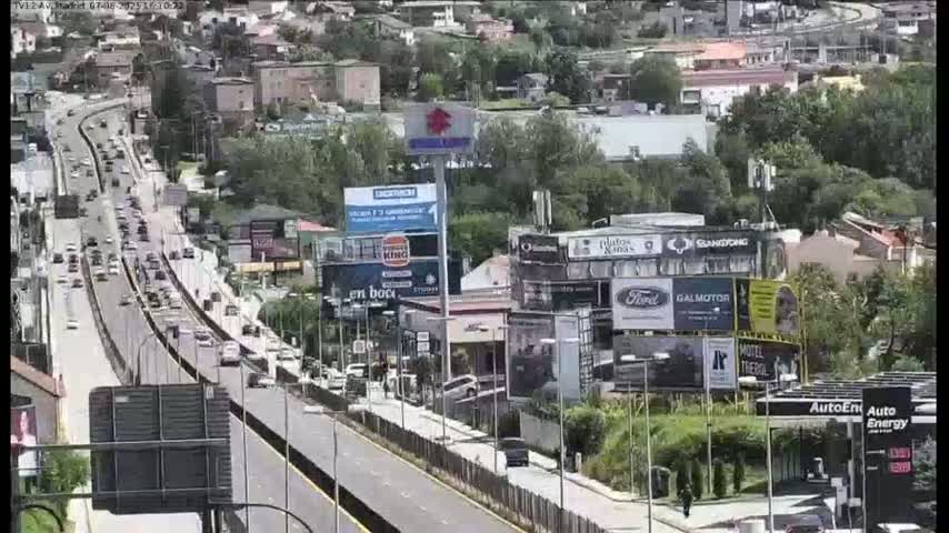 A highway with moderate traffic flows through a city on a partly sunny day, passing numerous billboards and buildings.