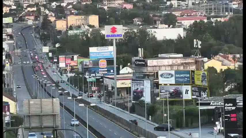 A highway with moderate traffic flows through a city with numerous billboards and buildings under a partly cloudy sky.