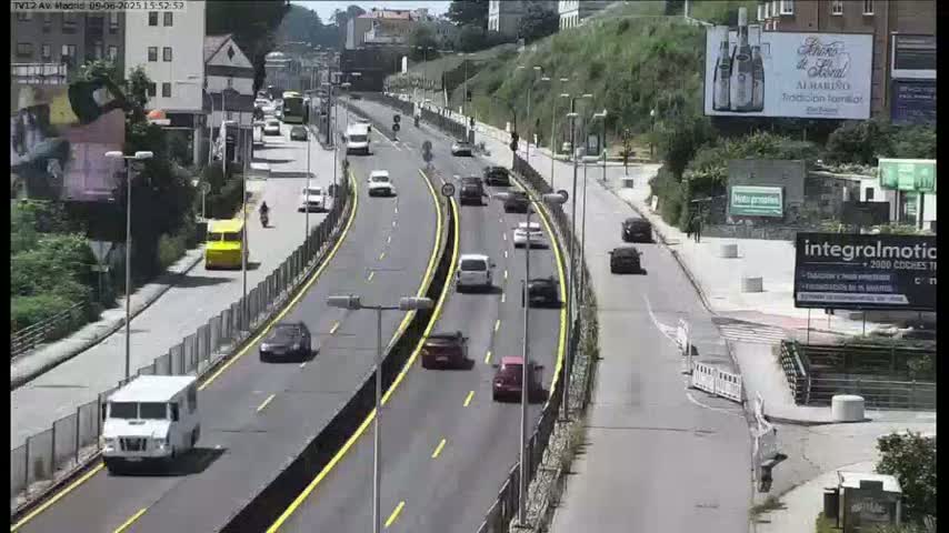 A multi-lane highway with moderate traffic flows through a hilly area on a sunny day.