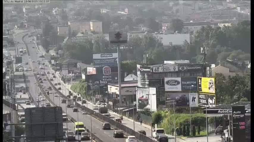 A hazy, sunny day shows a multi-lane highway with moderate traffic flowing past billboards and buildings.